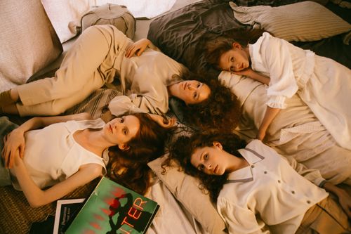Free Four women enjoying a relaxed sleepover, lying on a bed with pillows and books. Stock Photo