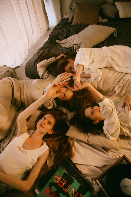 Free Four women lying together on a cozy bed in a warmly lit bedroom, sharing a relaxing moment. Stock Photo