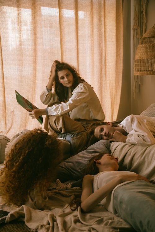Free A serene indoor scene with women relaxing on a bed, sharing moments under soft lighting. Stock Photo