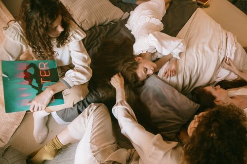 Free Four women in casual setting relaxing, reading, and bonding on a cozy bed. Stock Photo
