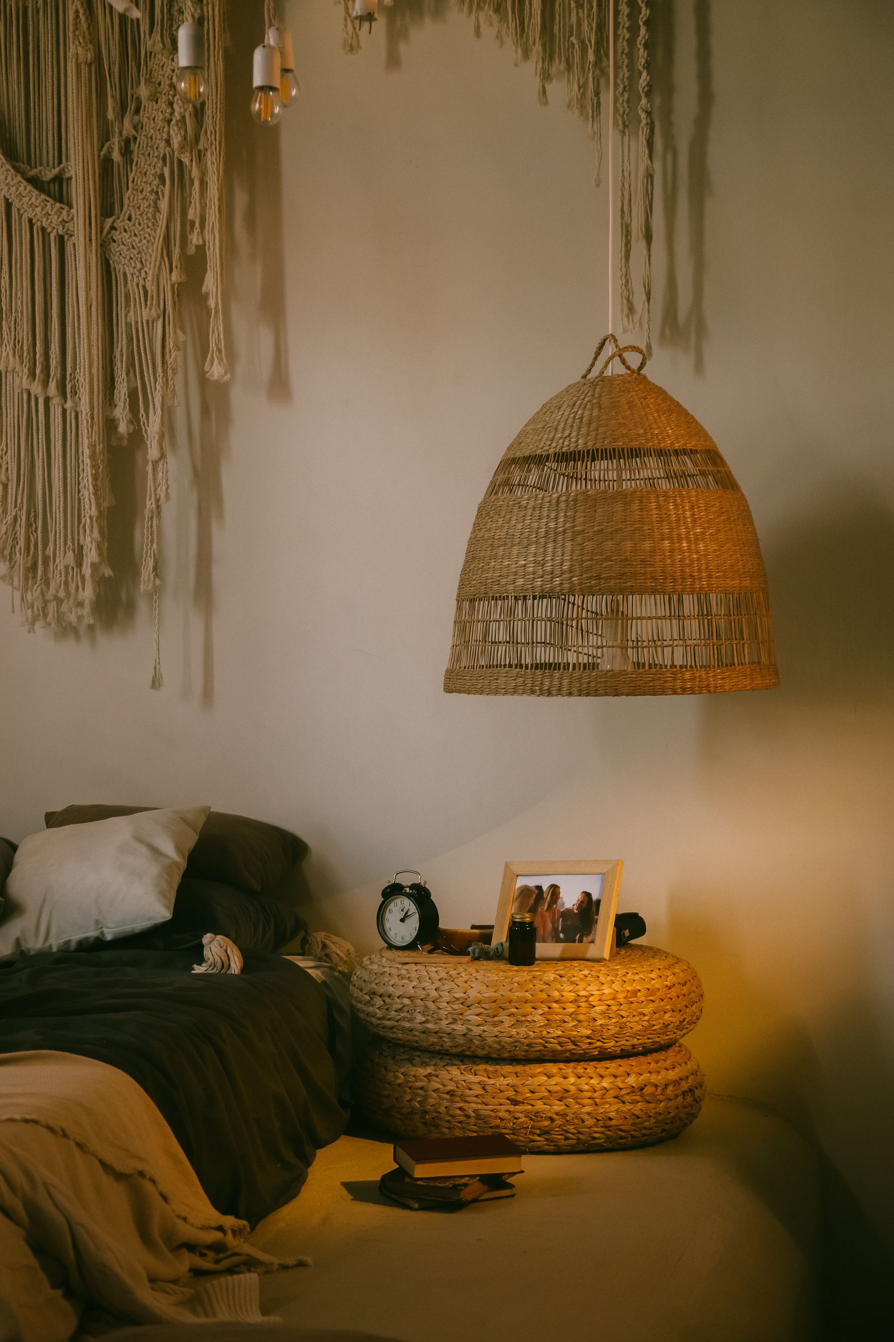 Boho bedside with a hanging woven lamp, wood table, alarm clock, textured bedding and macrame decor