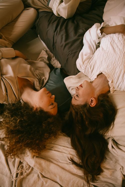 Free Two women lying down indoors, sharing a quiet and intimate moment in a cozy setting. Stock Photo