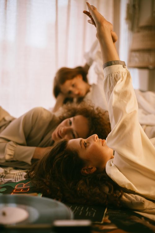 Free Three women enjoying a relaxed indoor sleepover, lying on a bed in comfortable attire. Stock Photo