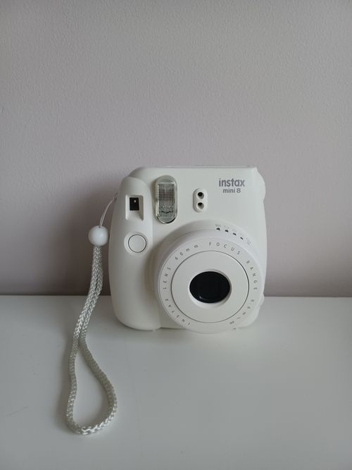 Free White instant camera with a strap against a neutral background, perfect for photography themes. Stock Photo