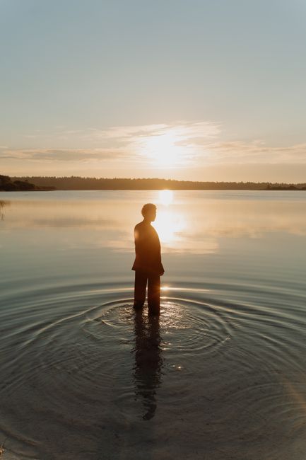 A silhouette of a person standing in a lake during a golden sunset, creating a serene reflection.
