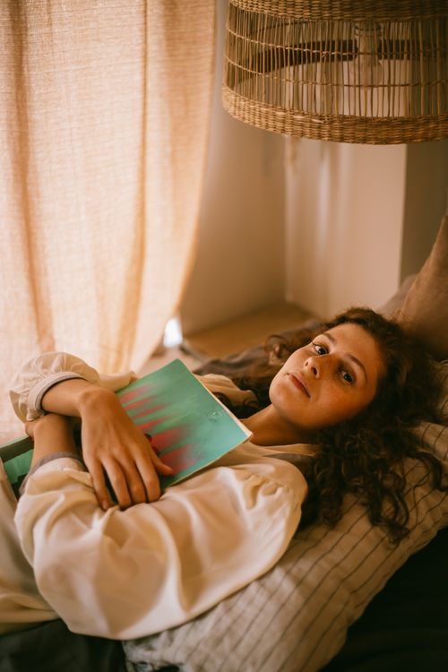 Free Teenager lying in bed with a book in a warm, cozy bedroom setting. Stock Photo