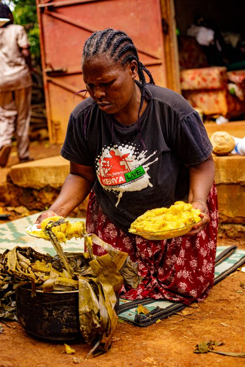 Free African woman kneeling outdoors, preparing a traditional Kenyan meal on plates. Stock Photo