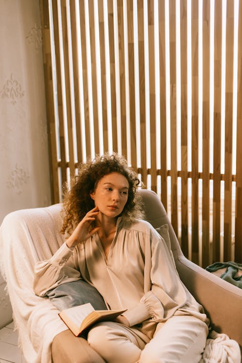 Pensive Redhead Woman Sitting in Chair with Book 