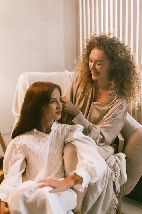 Woman Sitting in Armchair Braiding Teenage Girl Hair