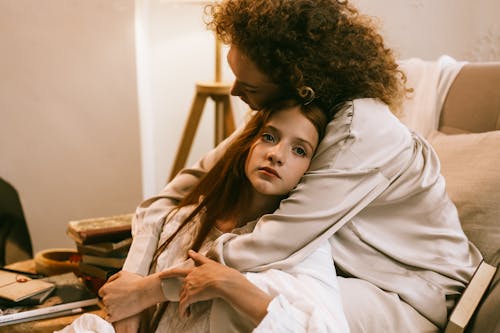 Woman Sitting in Armchair Embracing Teenage Girl