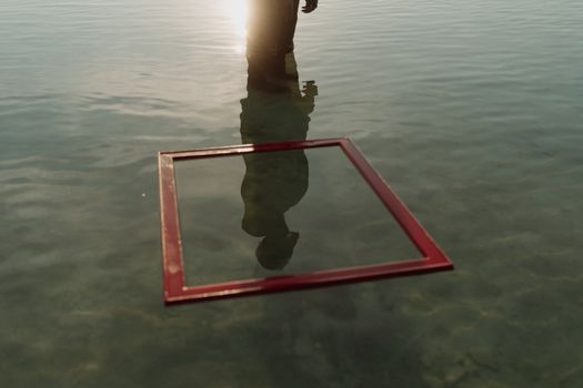 An artistic scene with a person standing in water, creating a unique reflection alongside a red frame.