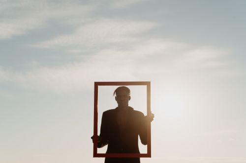 Free Artistic silhouette of a man holding a picture frame against a clear sky, symbolizing openness and creativity. Stock Photo