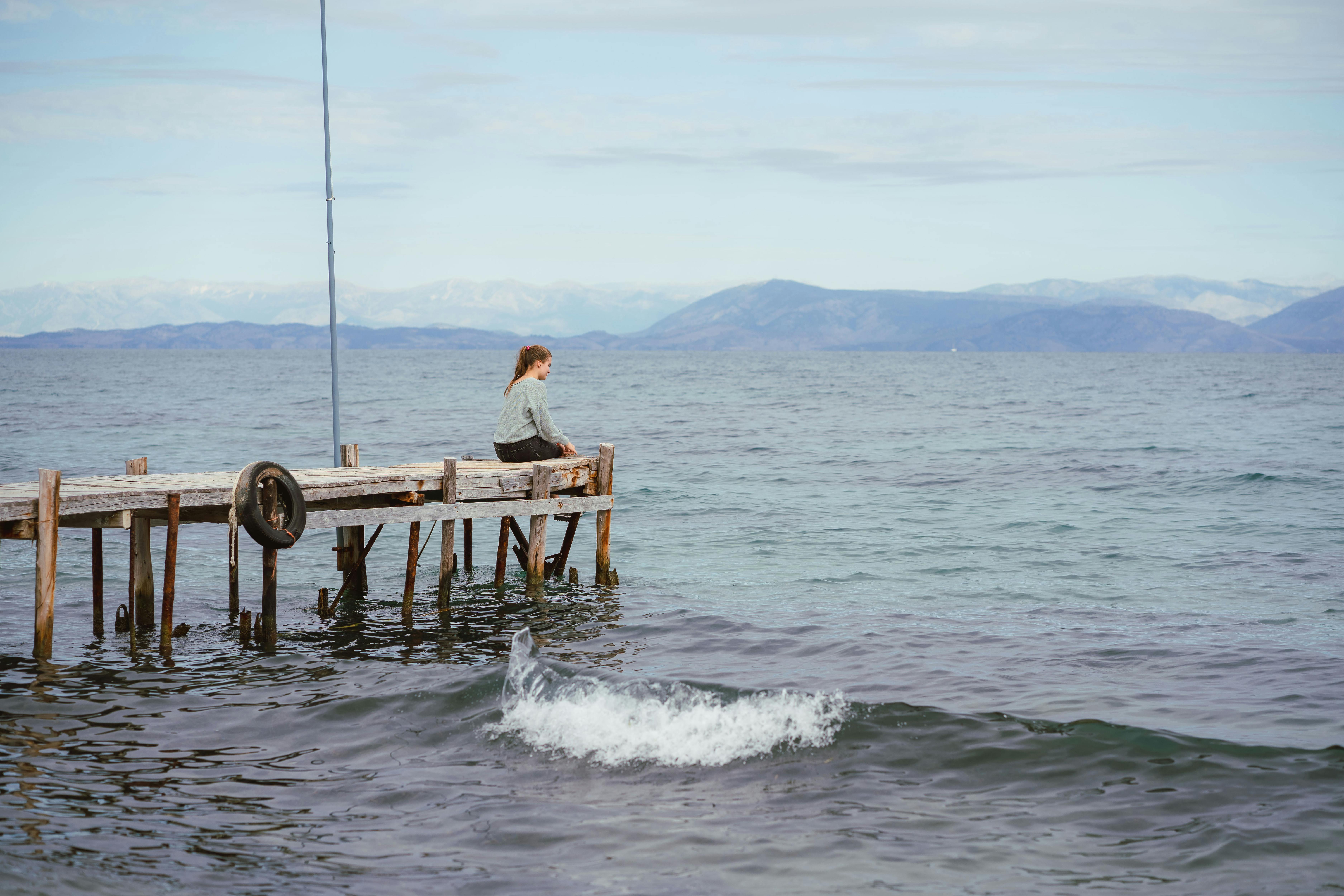 A serene scene of a woman sitting on a dock by the sea in Corfu, Greece.