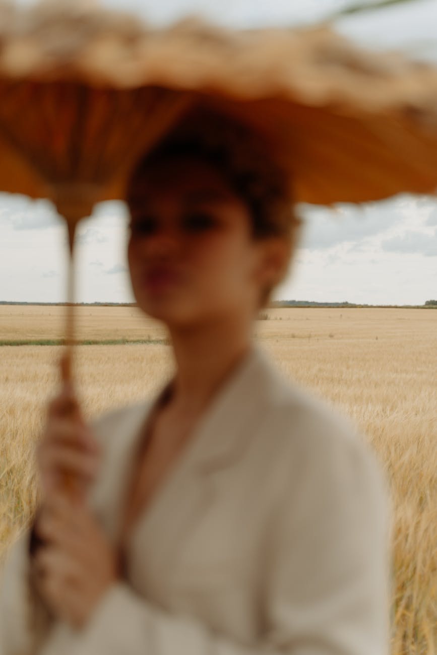 Artistic portrait of a blurred woman with an umbrella standing in a field, creating a dreamy aesthetic.
