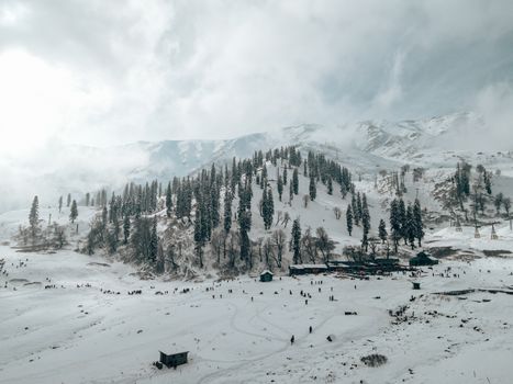 Aerial view of Gulmarg's snowy hills and scattered tourists during winter.