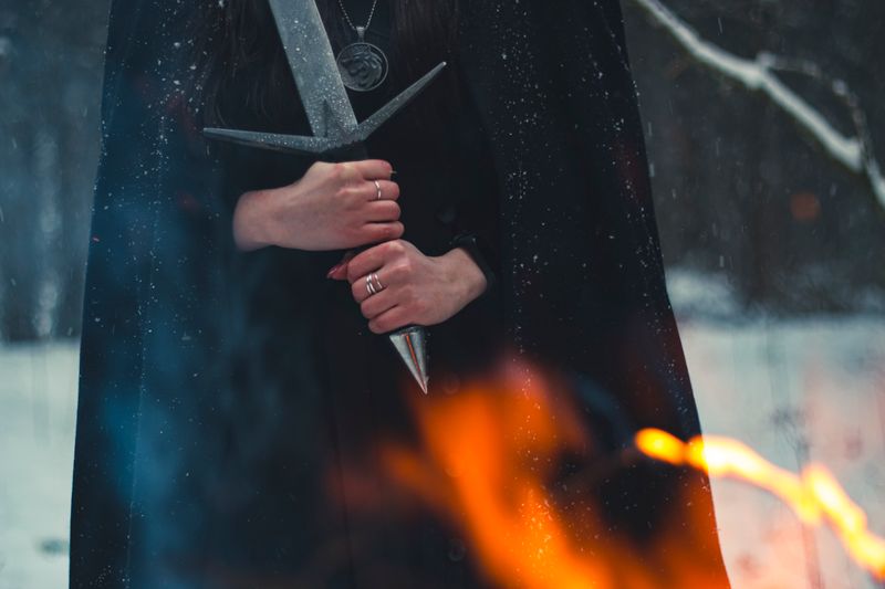 A cloaked figure holding a sword amid snow and firelight — photo by Vincuk Konan on Pexels