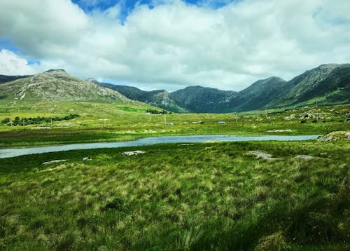 Green Grass Field near Mountains under the Cloudy Sky