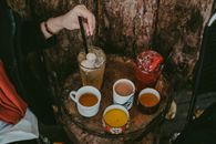 A Person Stirring a Cold Beverage on a Wooden Table with Assorted Drinks