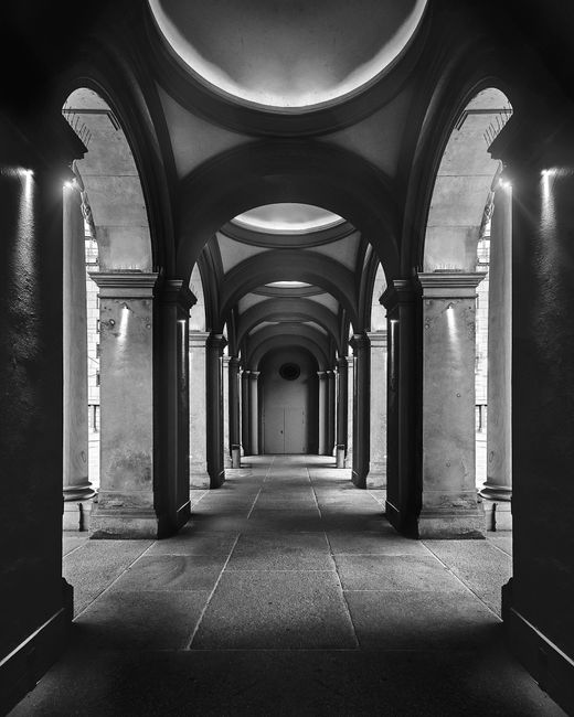 A dramatic black and white photograph of an ornate architectural hallway with arches.