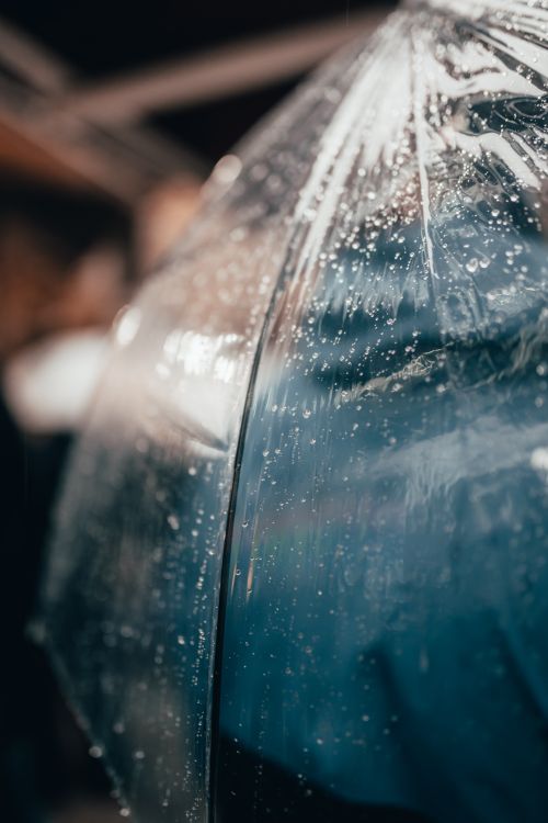 Free A close-up view of raindrops on a clear plastic umbrella, capturing gentle reflections and light. Stock Photo