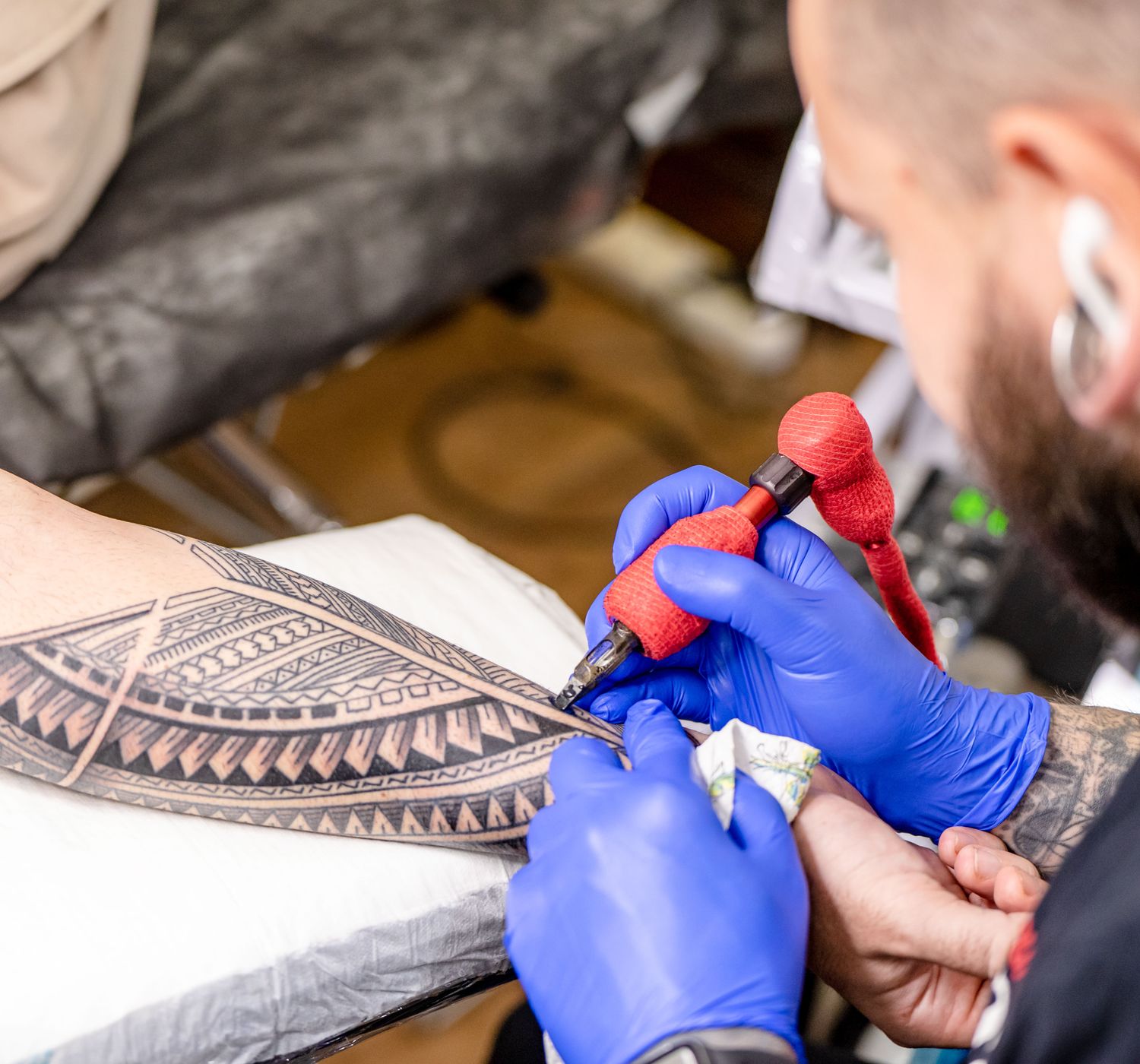 Close-up of a tattoo artist applying intricate design on a client's arm in a studio setting.