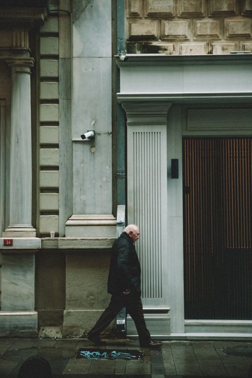 Free Elderly man in jacket walking along urban street with classic architecture. Stock Photo