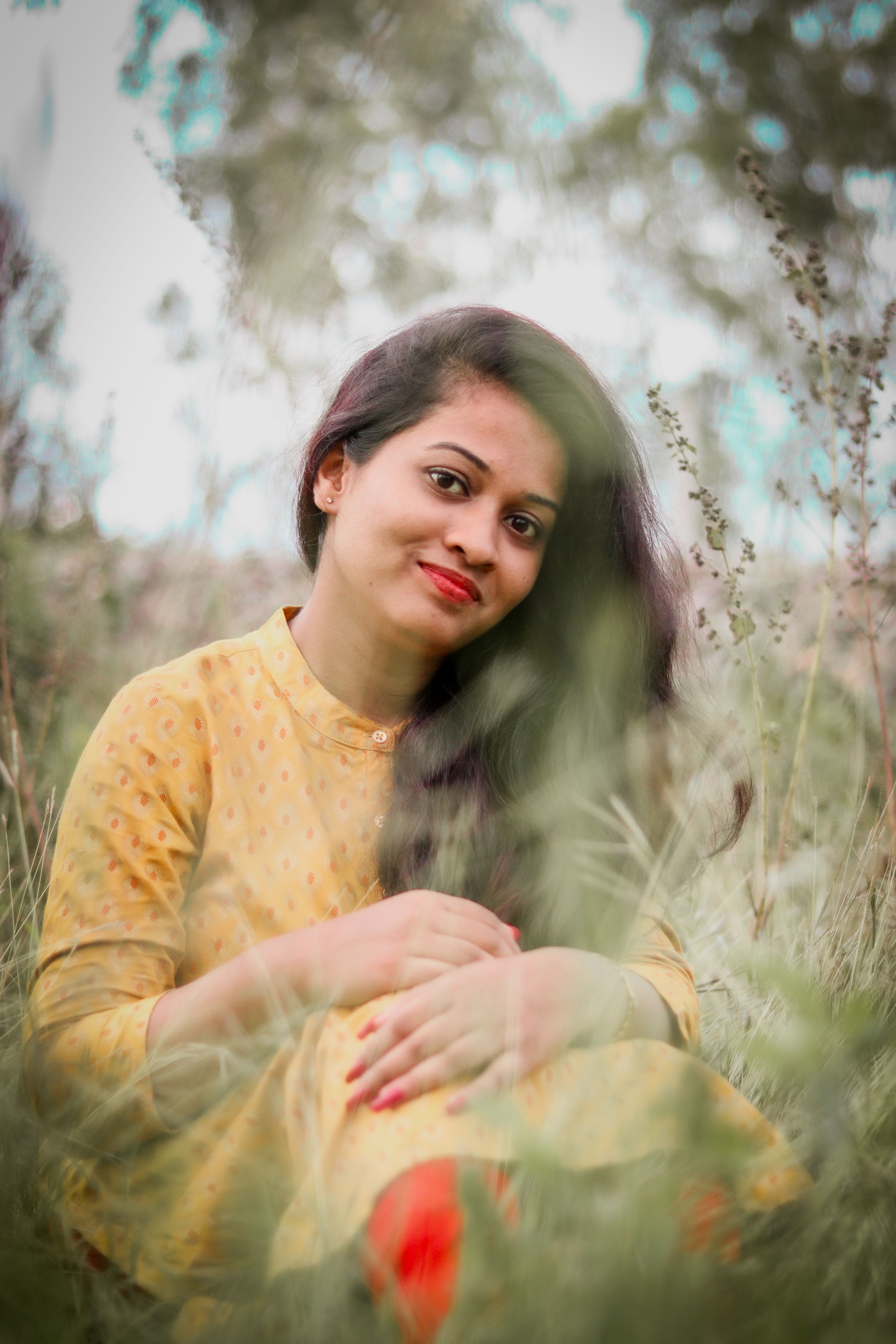 Portrait of a smiling woman sitting amidst grass in a tranquil meadow.