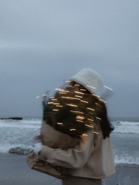 A dreamy image of a person holding glowing lights by the ocean on a cloudy day.