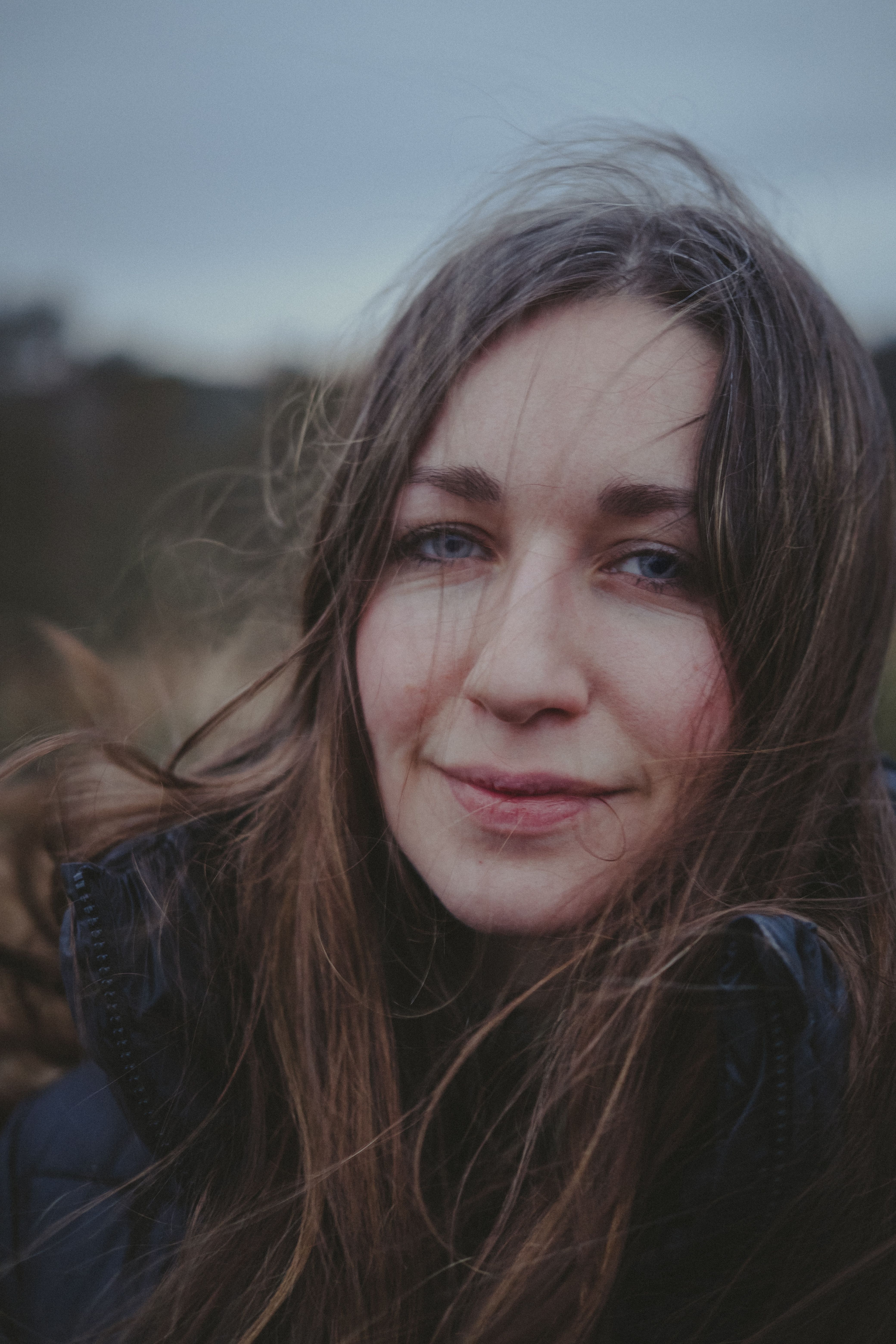Close-up portrait of a smiling woman with long hair outdoors, evoking natural beauty.