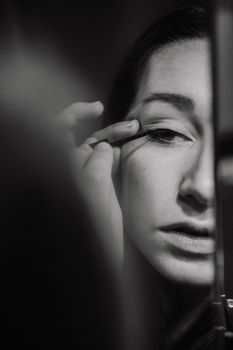 A close-up shot of a woman applying eyeliner in black and white.