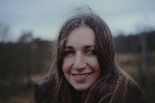 Free A serene close-up portrait of a woman smiling against a blurred outdoor background. Stock Photo
