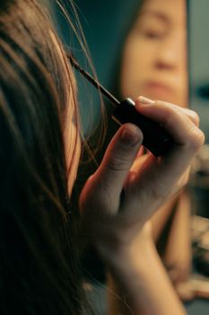 Close-up of a woman applying mascara, focusing on reflection in mirror.