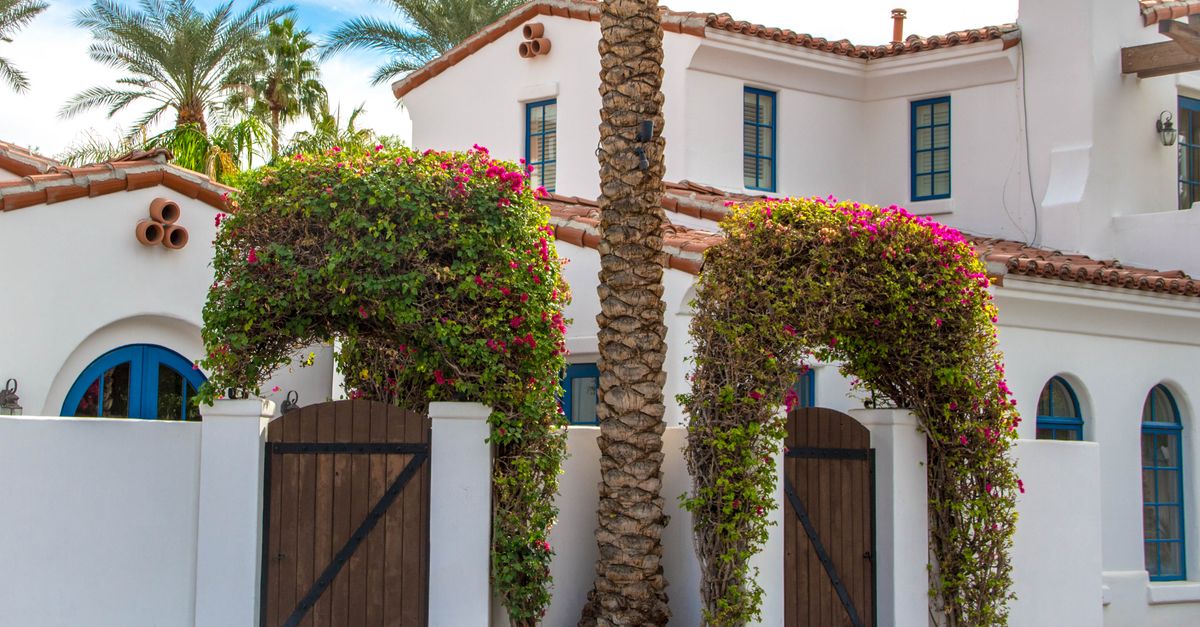 Elegant Mediterranean-style white villa with wooden doors and lush greenery in La Quinta, California.