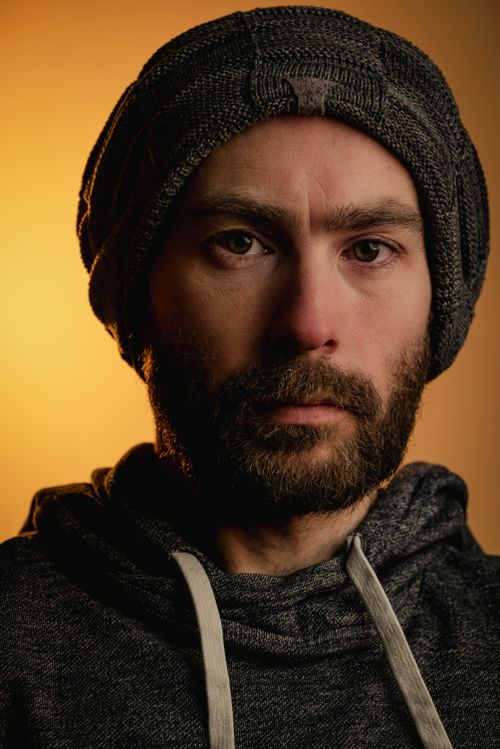 Free Close-up portrait of a bearded man wearing a knitted cap with a warm orange background. Stock Photo