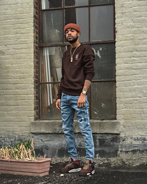 Free A Man in a Brown Sweater and Denim Pants Standing Near a Window Stock Photo