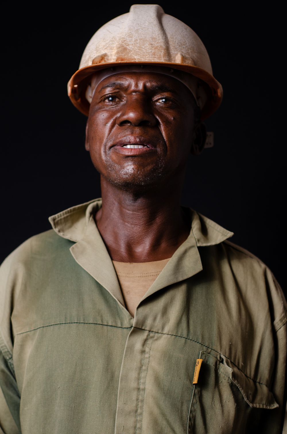 Tradesman in a hard hat and work overalls, photographed against a dark background.