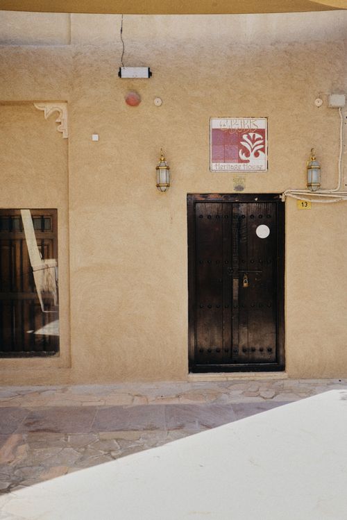 Free A rustic black wooden door set in a beige stucco facade under bright daylight. Stock Photo