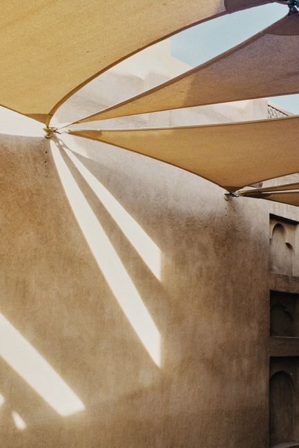 Geometric sunlight patterns on fabric cover create abstract shapes on a beige wall.