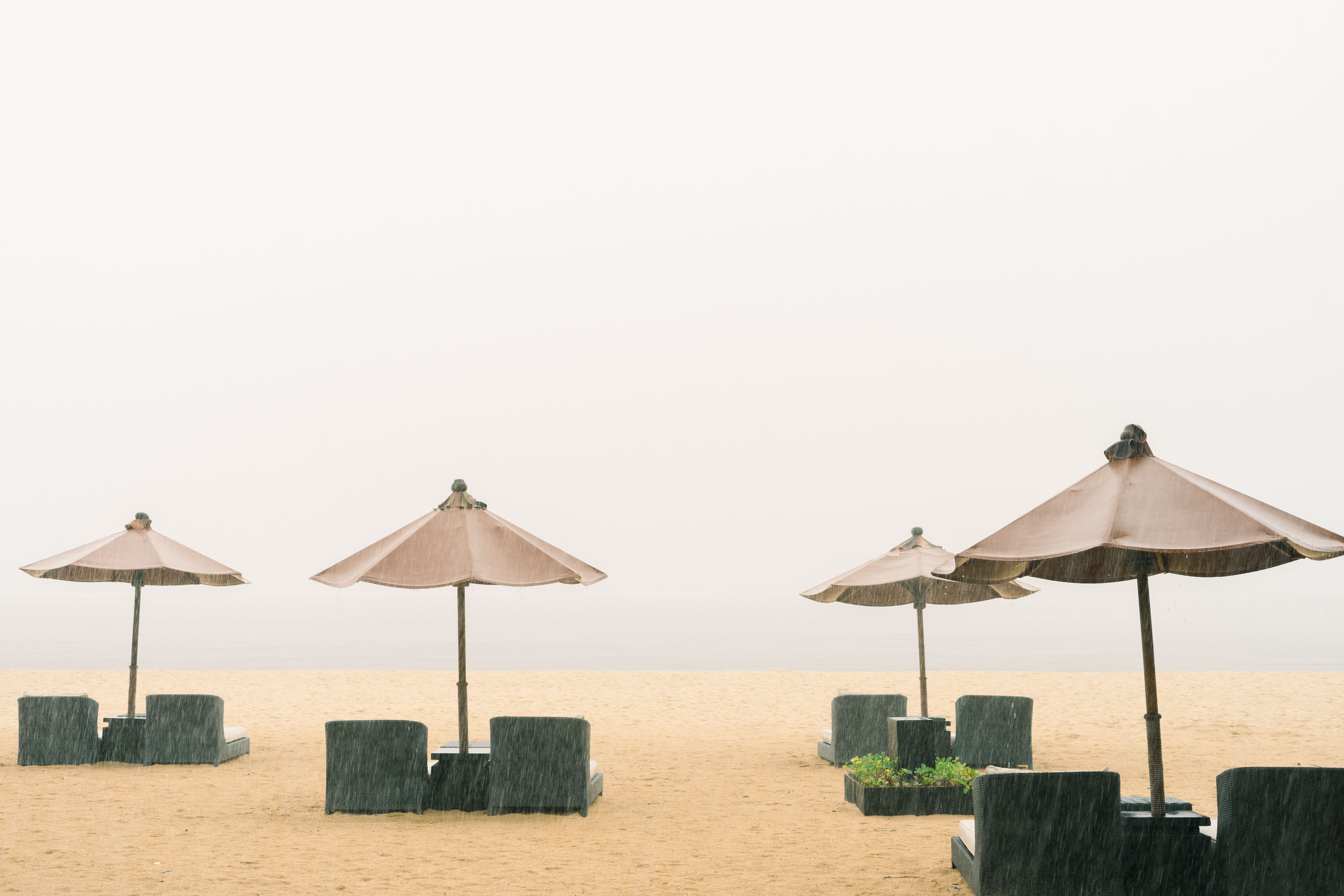 Deserted beach featuring umbrellas and loungers under rainfall, offering a serene and tranquil atmos