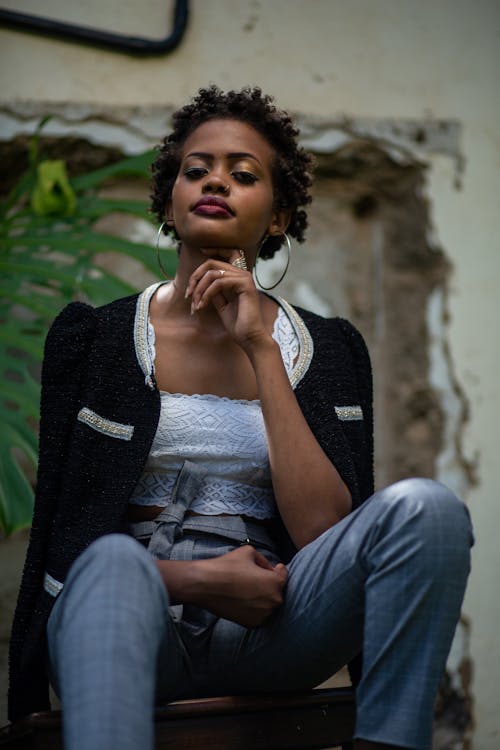 A Woman in Black Blazer Sitting on Wooden Chair while Looking at the Camera