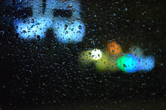 Vibrant bokeh lights seen through rain-covered glass, creating a moody night scene.