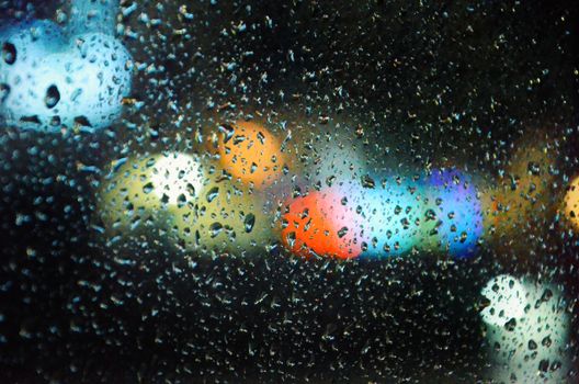 Raindrops on a window with vibrant bokeh lights create an abstract yet colorful night scene.