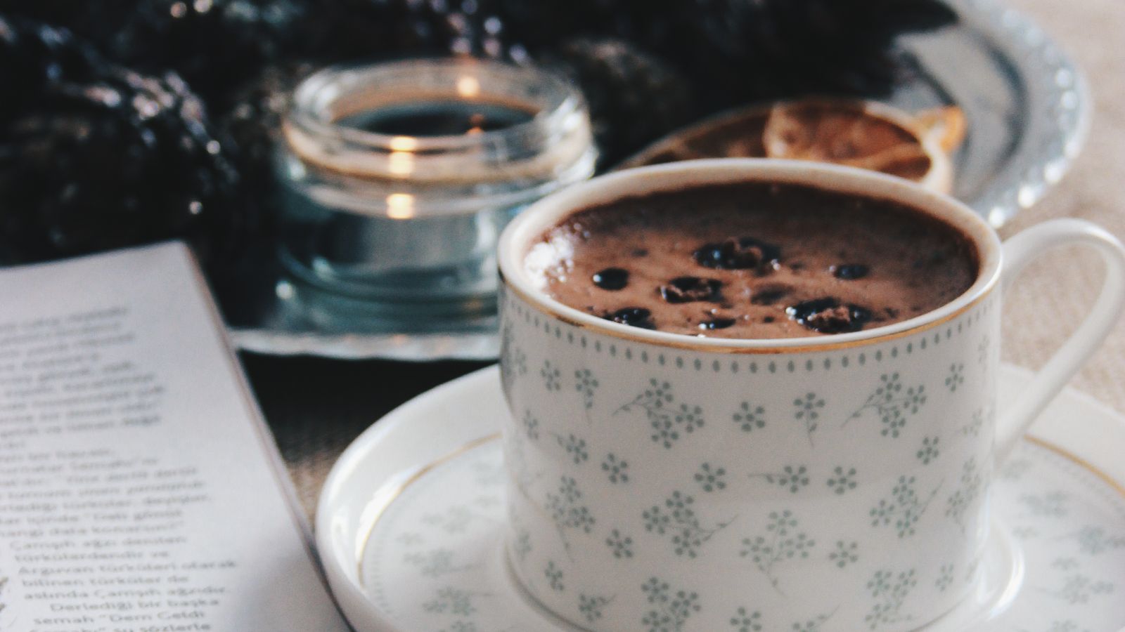 A patterned coffee cup beside a candle and an open page