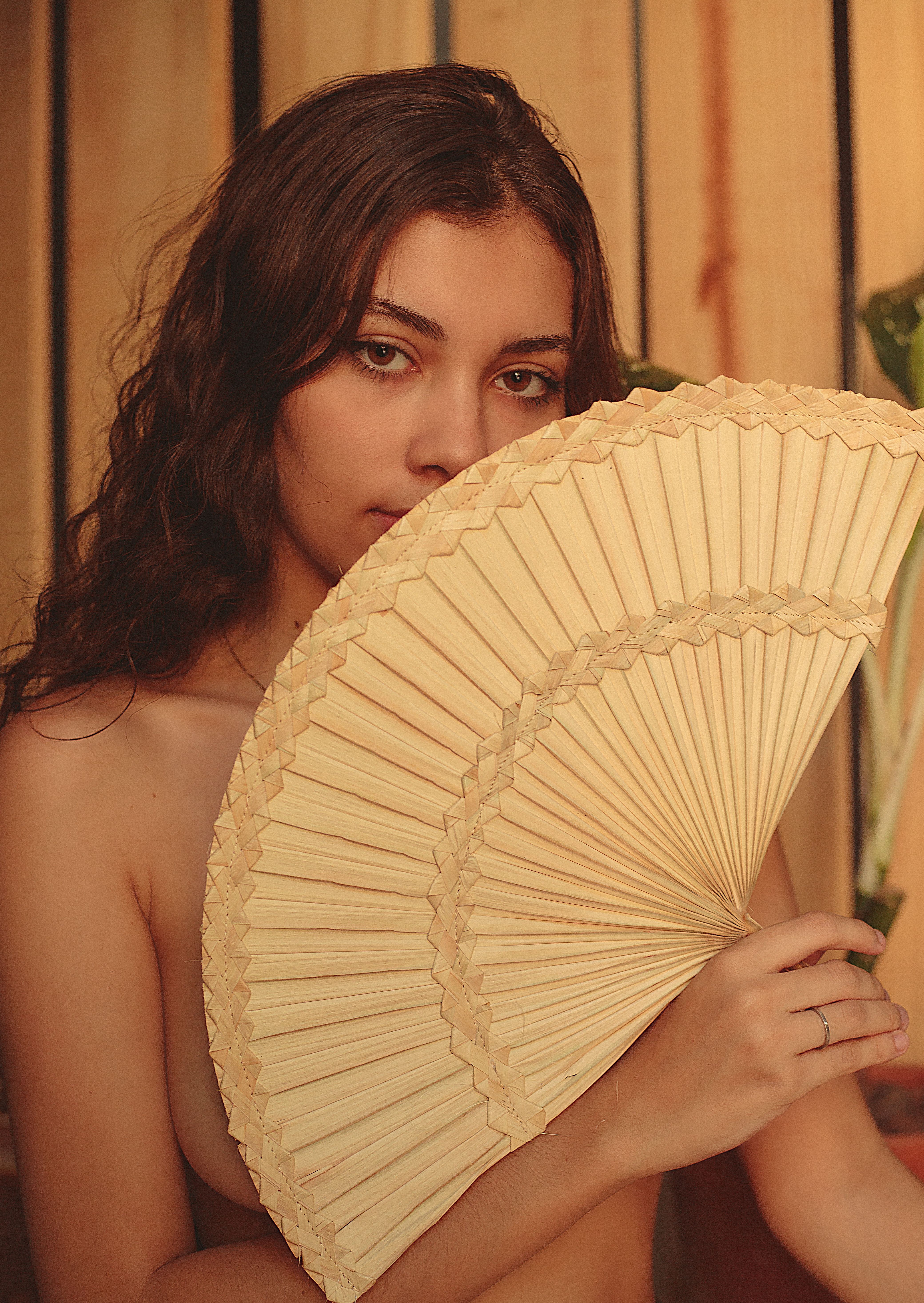 Portrait of a young woman elegantly holding a lace hand fan indoors.