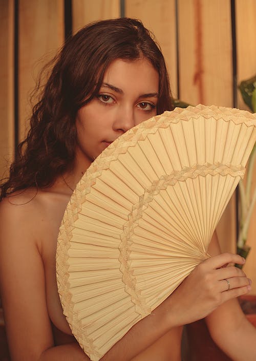 A Woman Covering Her Face With Beige Hand Fan
