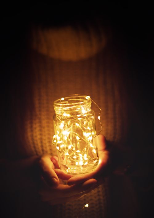 Free Cozy hands hold an illuminated jar of string lights, creating a warm ambient glow. Stock Photo