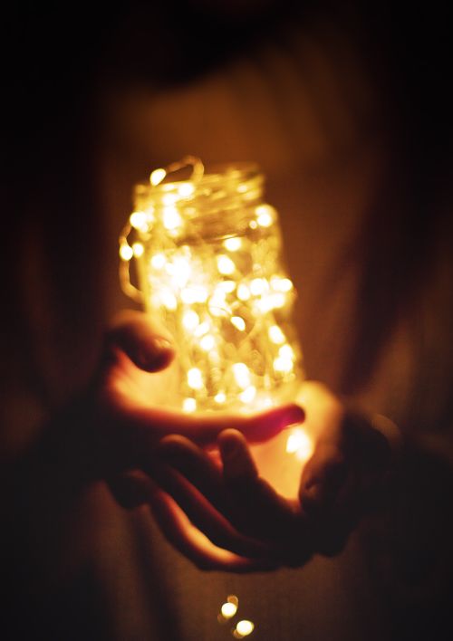 Free Enchanting hands holding an illuminated glass jar filled with warm string lights, creating a magical glow. Stock Photo