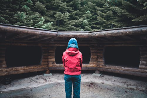 Free Person in Red Hoodie Standing Near Brown Wooden House Stock Photo