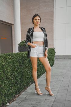 Elegant woman in a striped blazer and shorts posing confidently in an urban setting.