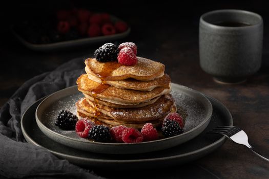 Stack of pancakes with fresh berries and coffee, captured in a moody setting.